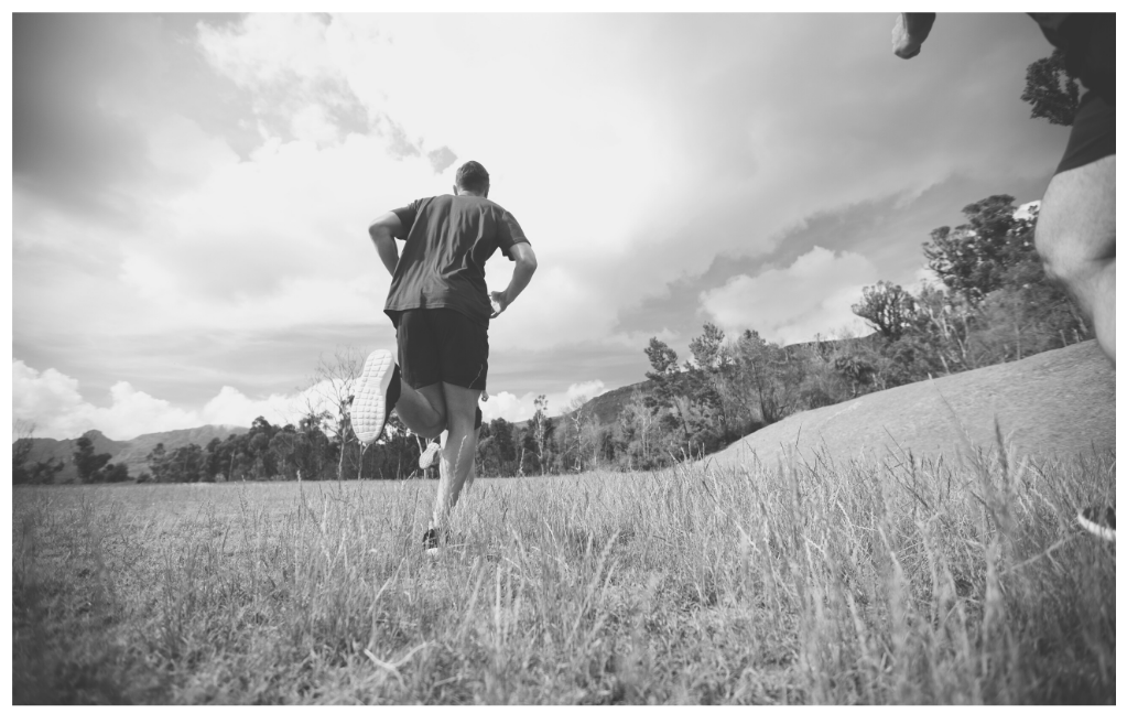 Get fit! Black and white image of a man running in a field towards some trees. 